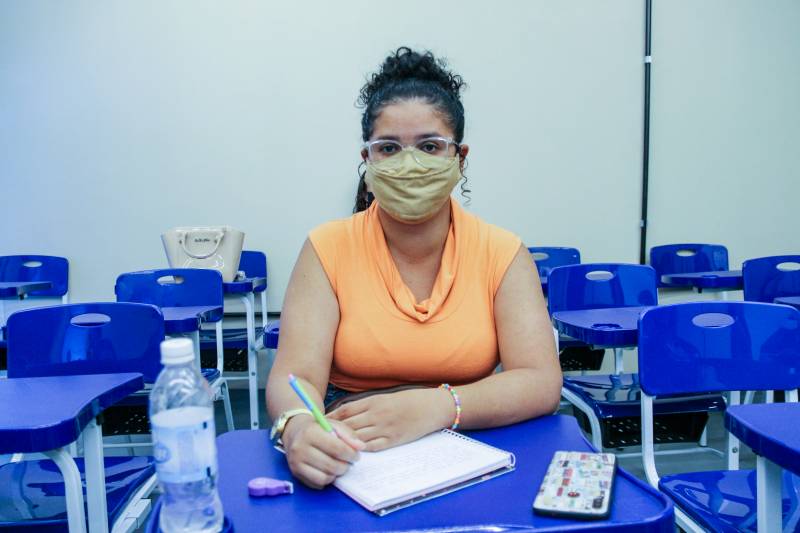  Luana Marinho: blusa amarela, mascara bege, escrevendo no caderno com caneta verde