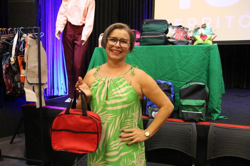 Edilene: moça de óculos, vestido verde, cabelo curto, segurando uma bolsa 