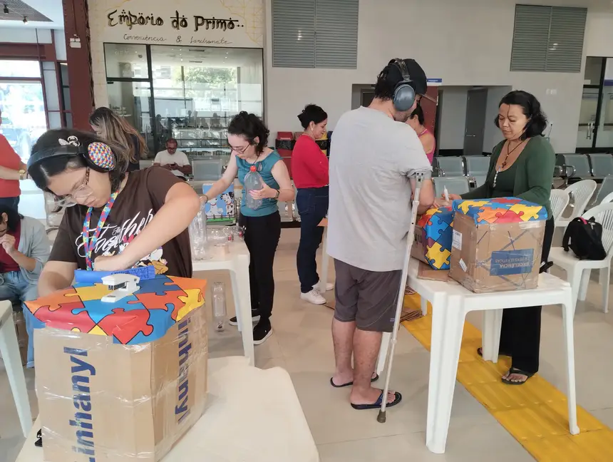 Participantes da oficina, incluindo mães atípicas e seus filhos, trabalham na decoração dos puffs